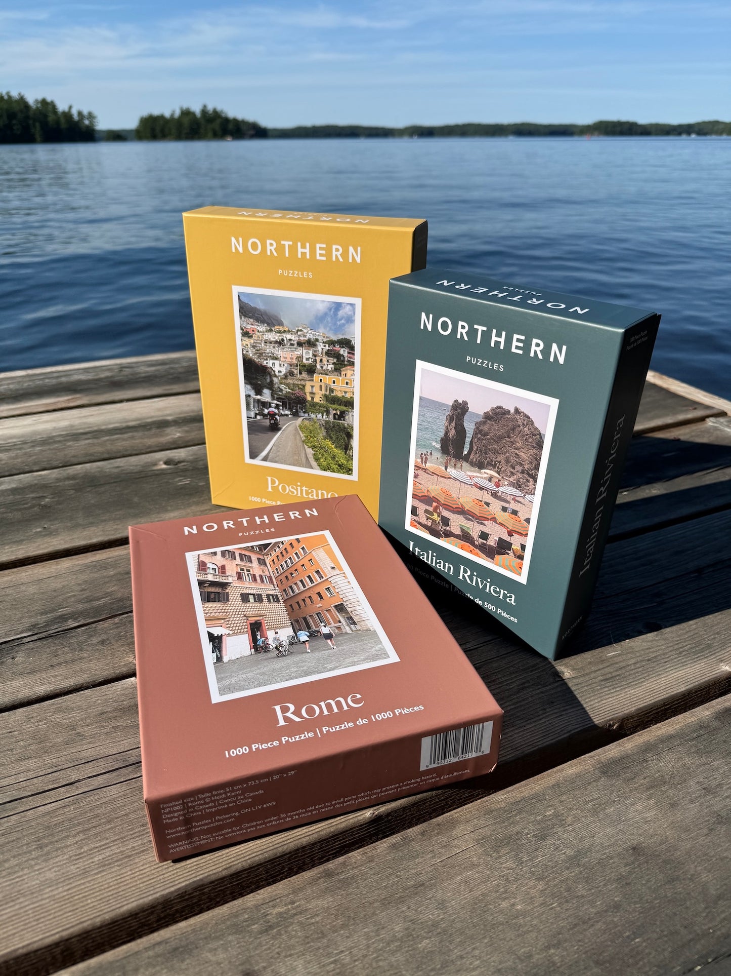 Three travel-themed books on a wooden dock by a lake